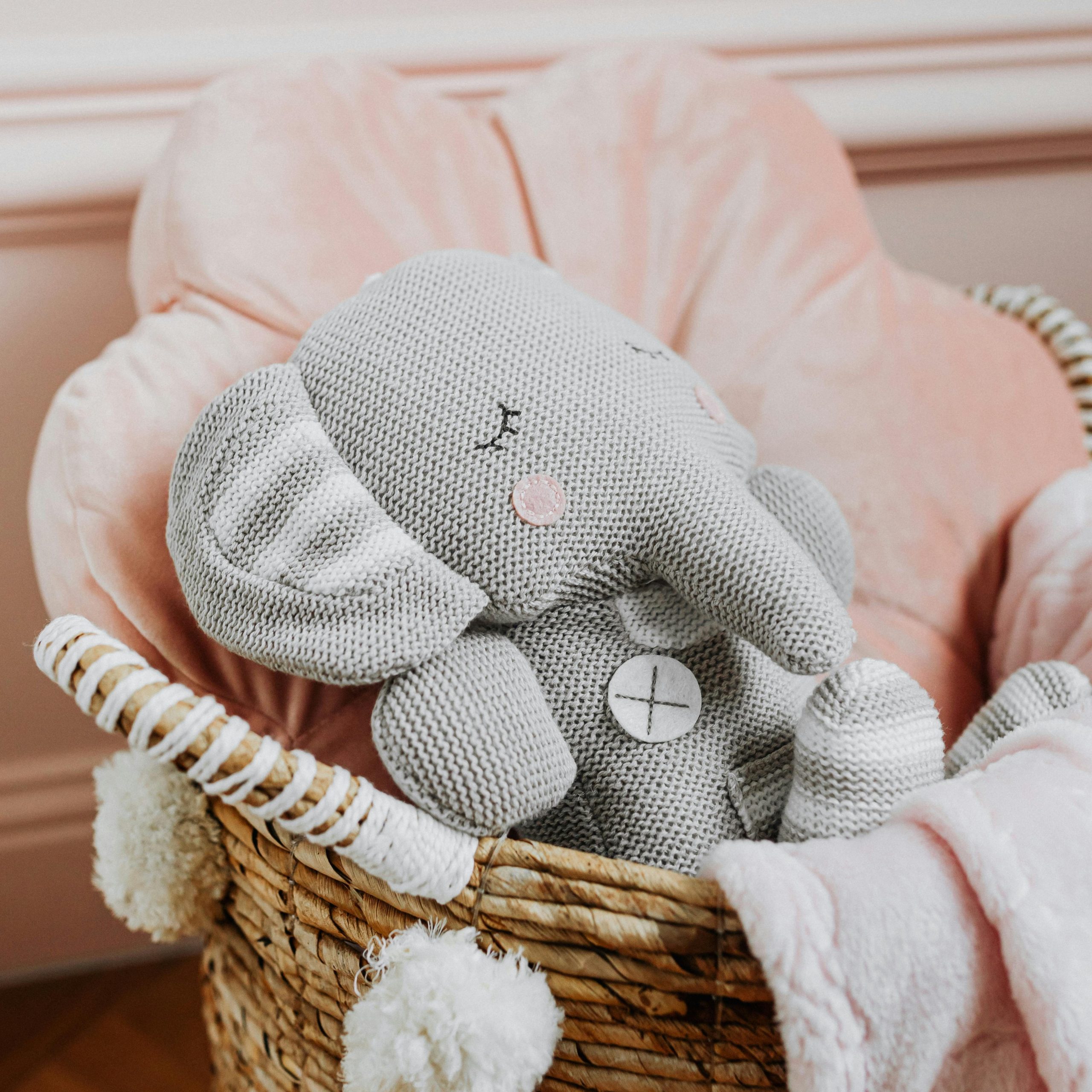 Adorable stuffed elephant toy nestled in a soft woven basket with pink lining.